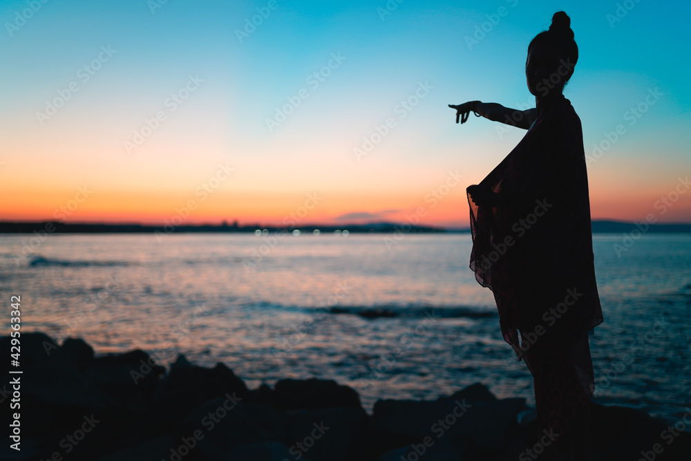 Silhouette of woman pointing forward at sunset during golden hour