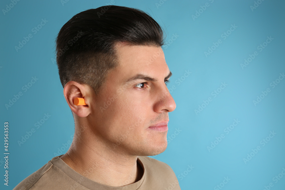 Man wearing foam ear plugs on light blue background Man wearing foam ear plugs on light blue background