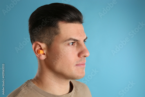 Man wearing foam ear plugs on light blue background