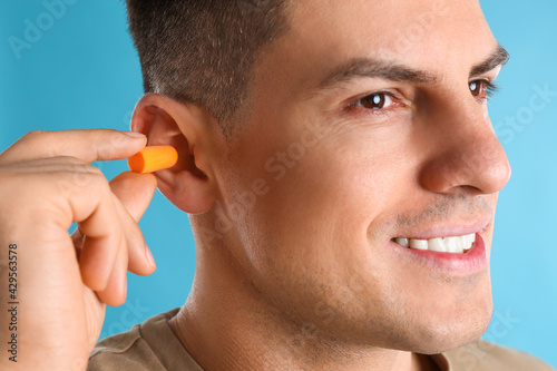 Plakat Man inserting foam ear plug on light blue background, closeup
