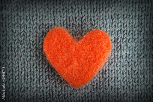 A red heart made of wool lies on a gray knitted background.The concept of handwork, needlework and needlework.Background for Valentine's Day, Birthday, Mother's Day.Top view.Flat styling style