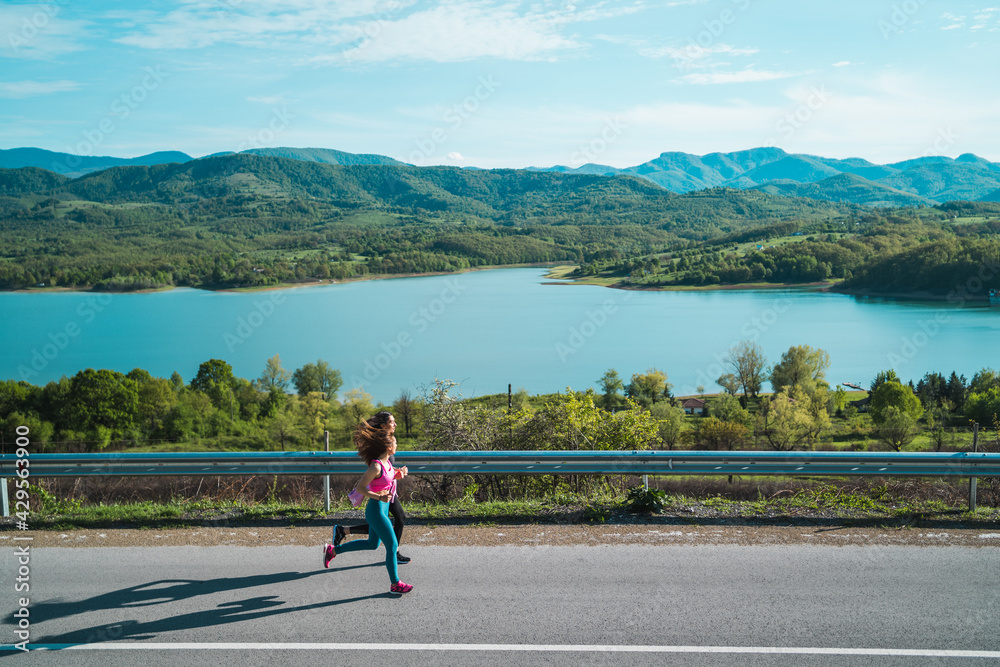 Women jogging together near lake, practicing for healthy lifestyle