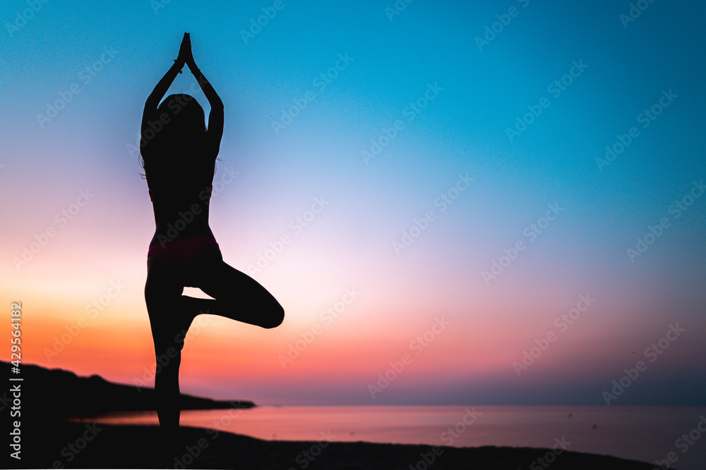 Silhouette Athletic Woman Doing Yoga on The Beach against bright colorful sunset