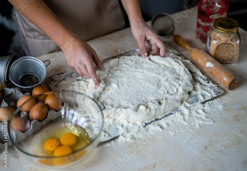 Hands of a girl on a wooden table in an apron knead the dough. Around the flour, eggs, salt.