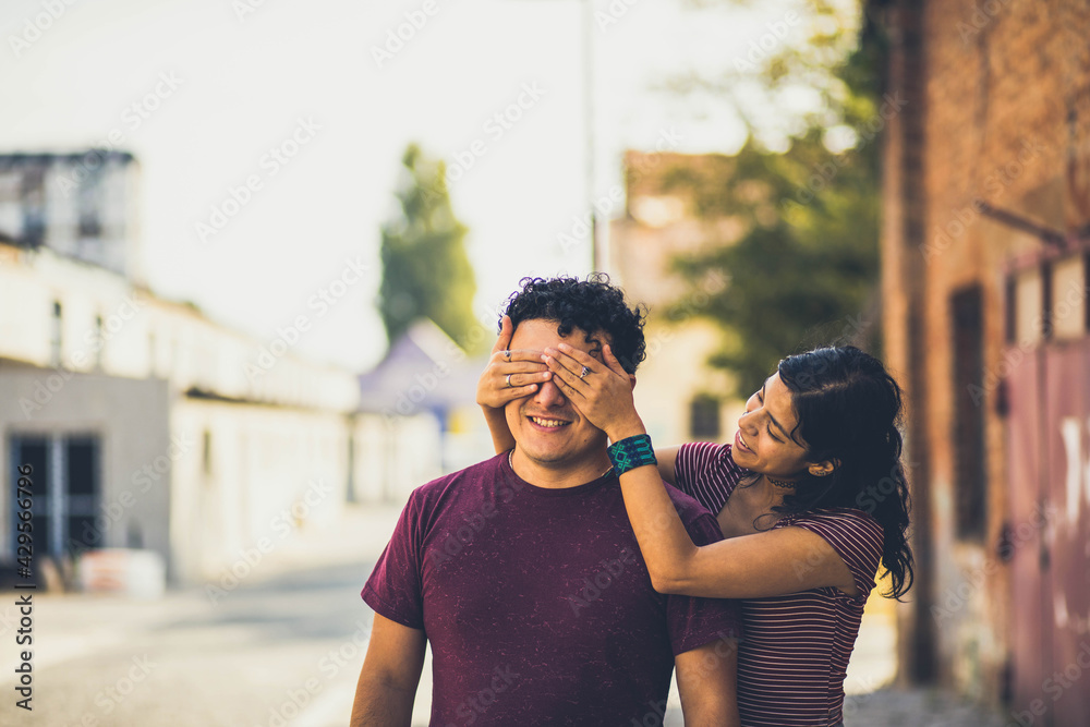 Young couple on the street. Girl holding hands on eyes to her boyfriend.