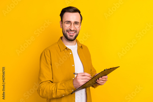 Photo of cute positive young guy wear casual clothes glasses smiling signing contracts isolated yellow color background