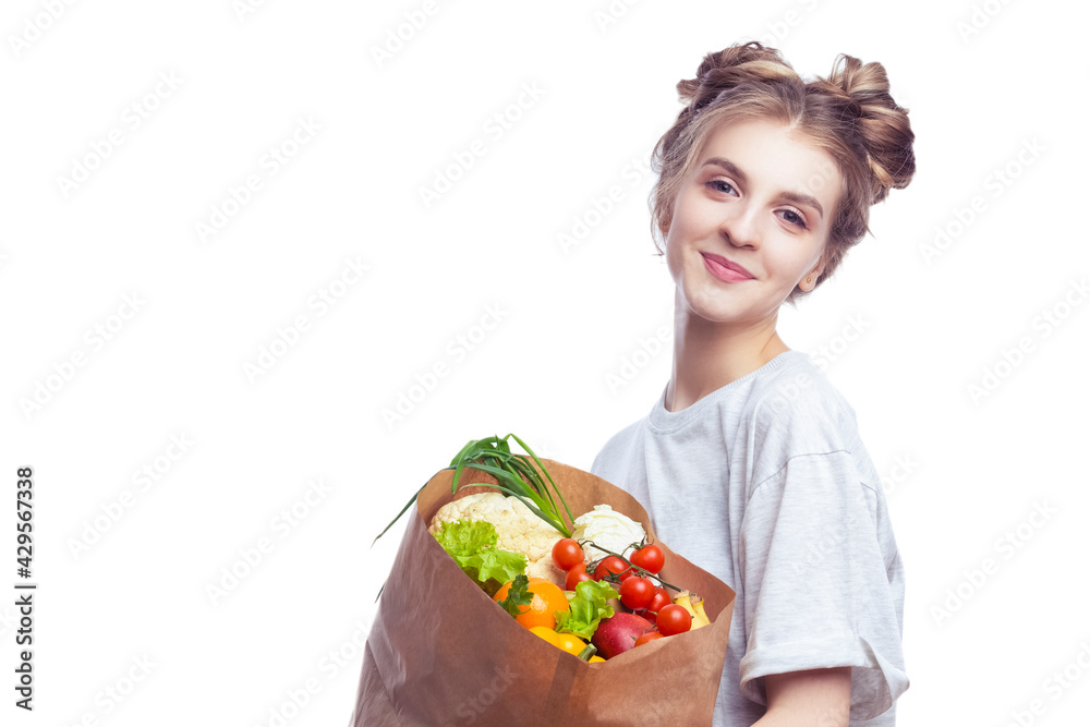 Vegetarian Eating Ideas. Portrait of Young Caucasian Girl With Eco Paper Bag Filled With Multiple Vegetables and Groceries Posing With Smile Against White Background. Vegetarian Eating Ideas. Portrait of Young Caucasian Girl With Eco Paper Bag Filled With Multiple Vegetables and Groceries Posing With Smile Against White Background.