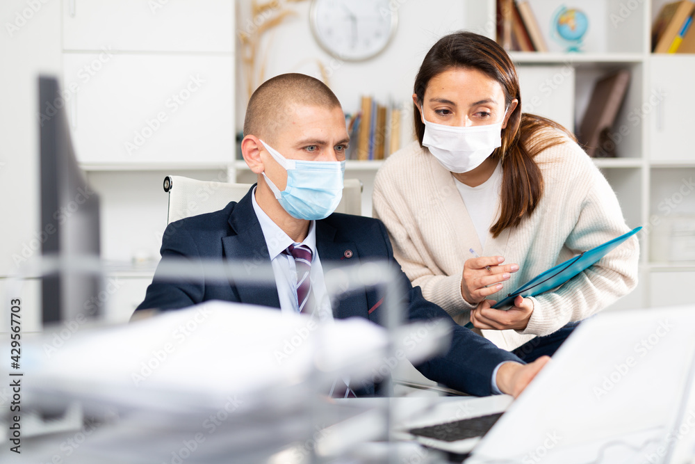 Corporate business coleagues businessman and businesswoman in face masks discussing something and working together in modern office
