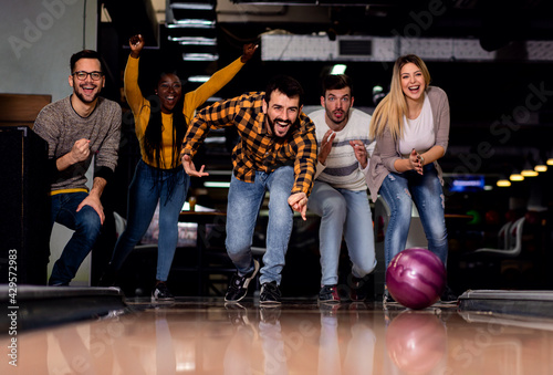 Group of friends enjoying time together laughing and cheering while bowling at club.