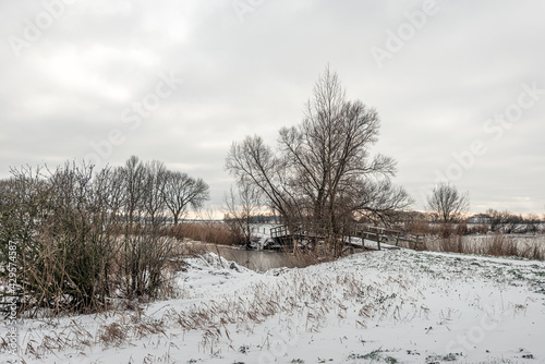 Simple wooden bridge in a snowy winter landscape. The photo was taken on a cloudy day in the Dutch province of North Brabant. © Ruud Morijn