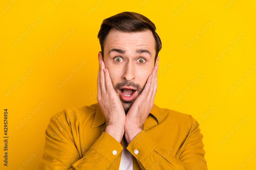 Photo of young handsome man amazed shocked surprised hands touch cheeks isolated over yellow color background Photo of young handsome man amazed shocked surprised hands touch cheeks isolated over yellow color background