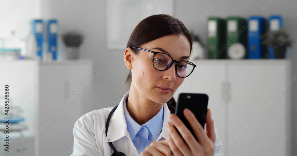 Happy female doctor using smartphone in medical office
