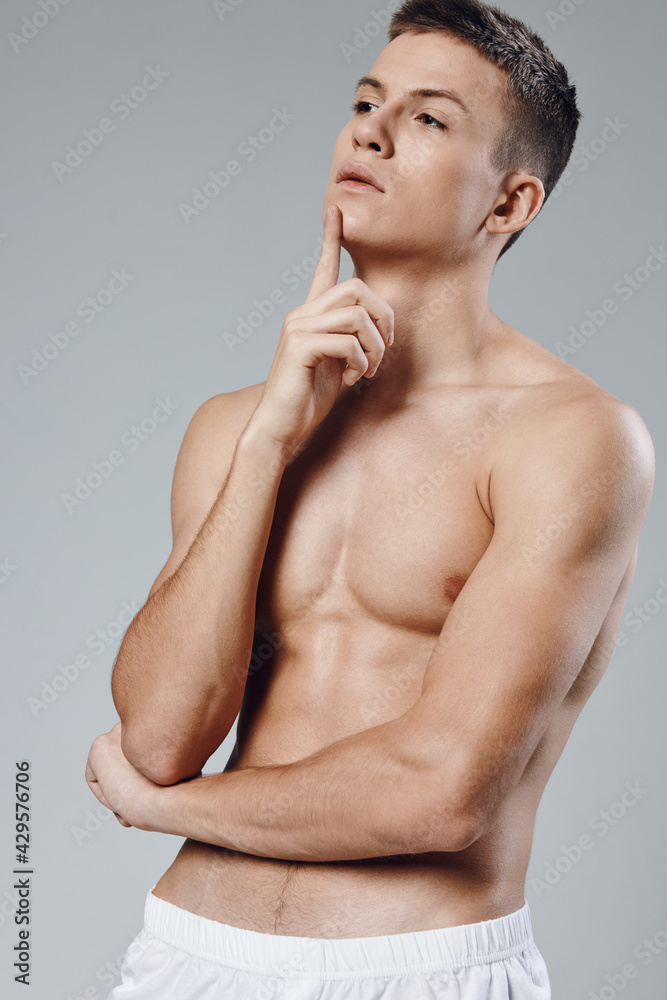 Fototapeta premium athlete with a pumped-up torso holds his hand near his face and cubes on his stomach gray background model