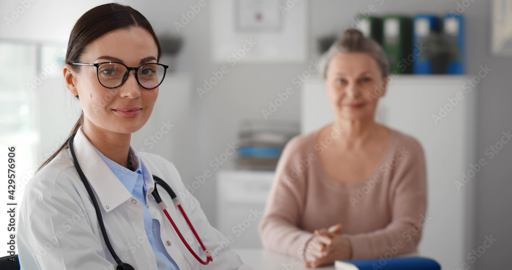 Portrait of young woman doctor and aged patient smiling at camera in clinic office Portrait of young woman doctor and aged patient smiling at camera in clinic office