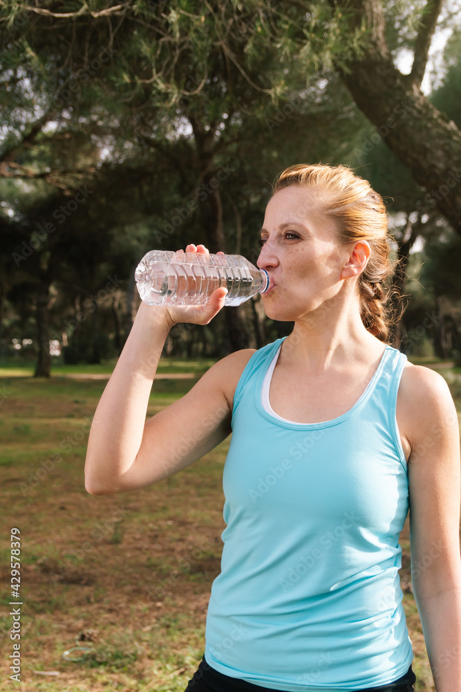 Vertical photo of a Hispanic woman drinking cold water after a hard workout outdoors. Healthy lifestyle, with top copy space. Vertical photo of a Hispanic woman drinking cold water after a hard workout outdoors. Healthy lifestyle, with top copy space.
