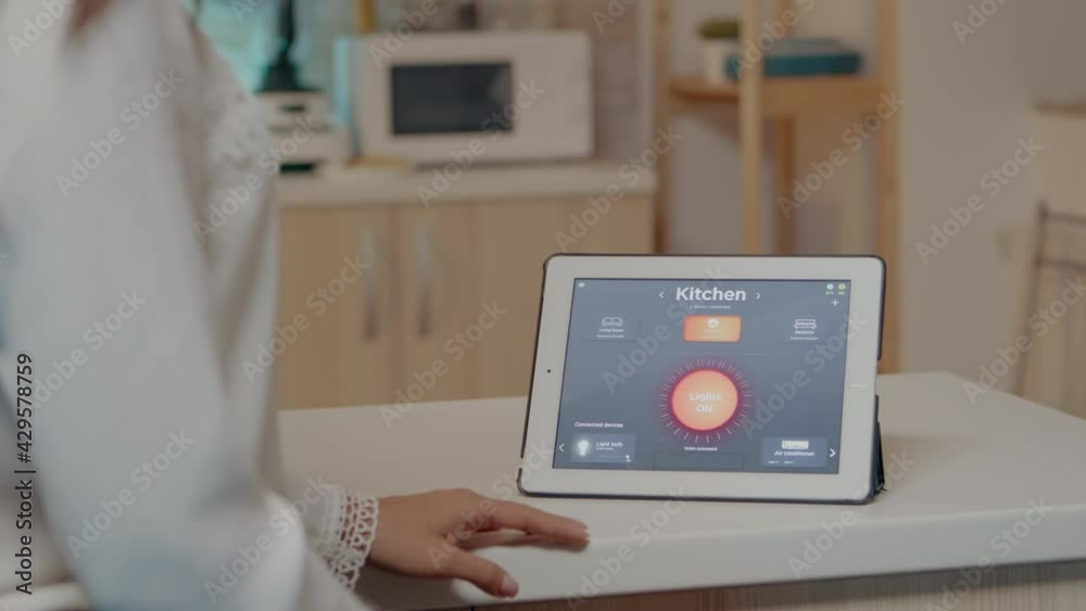 Young woman using smart home application with voice command to turn on the light by tablet. Lady using lighting control app in modern house with automation system controlling efficiency of energy Young woman using smart home application with voice command to turn on the light by tablet. Lady using lighting control app in modern house with automation system controlling efficiency of energy