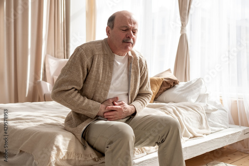 Foto Senior man having stomach pain sitting at home.