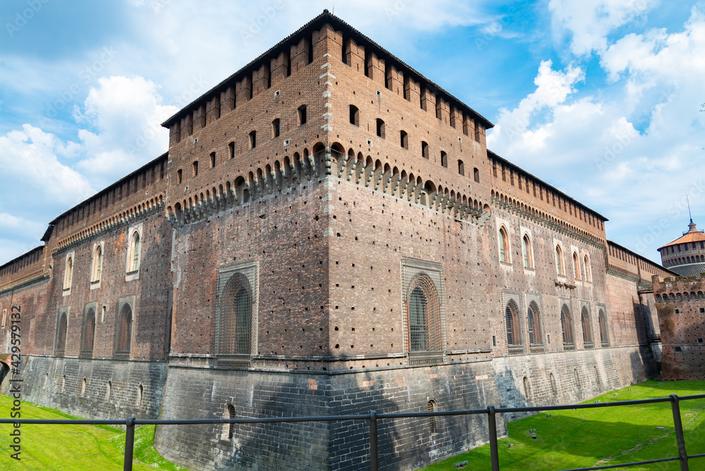 Corner of the defensive walls of the famous Castello Sforzesco (meaning: Sforza's Castle) in Milan, Italy. Blue sky and white clouds in the background.