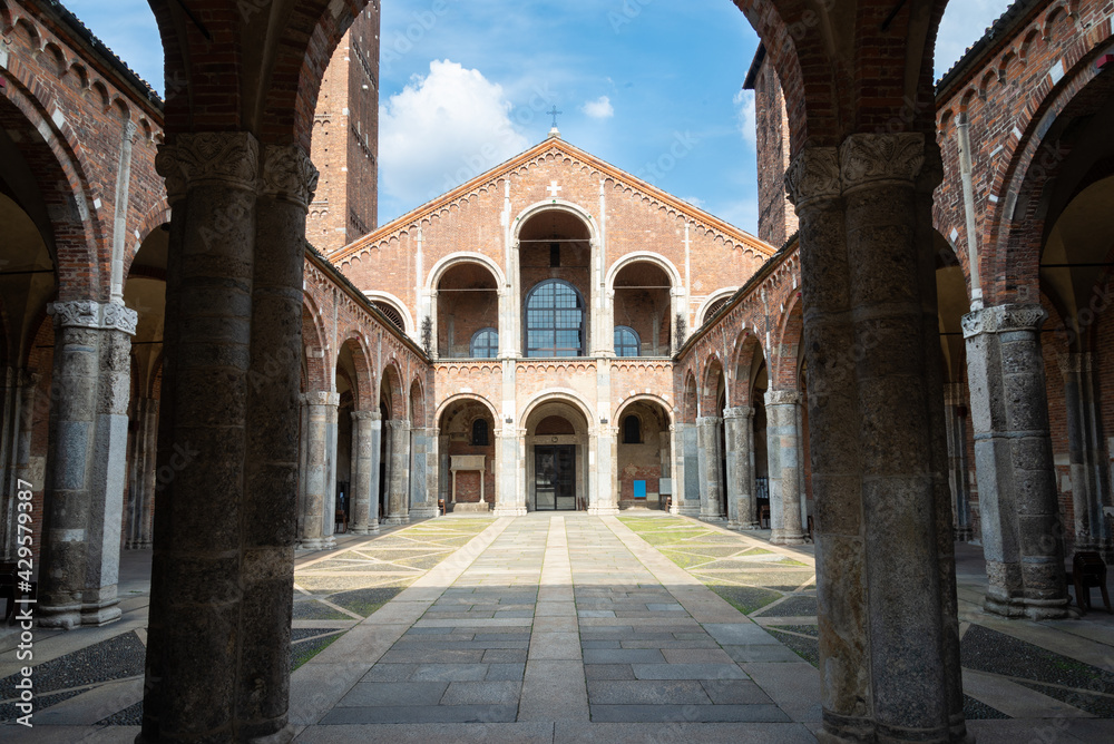 Columns silhouette of the famous Sant'Ambrogio (meaning Saint Ambrogio) romanic cathedral in Milan, Italy. The patio and the facade with symmetrical arches in the background.