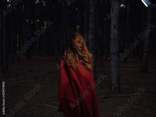 A woman travels in the forest at night with a red plaid on her shoulders, back view