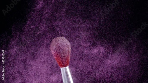 Makeup brush shudders and creates a swirl of fine particles of pink powder against a black background, slow motion, 300fps.