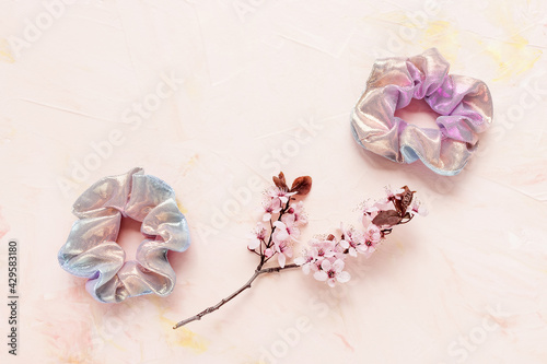 Fototapeta Naklejka Na Ścianę i Meble -  Twoshiny scrunchies and fresh spring branch with pink flowers on pastel backround. Flat lay, top view. Diy accessories, hairstyle, lifestyle, spring and summer outfit ideas concept, copy space