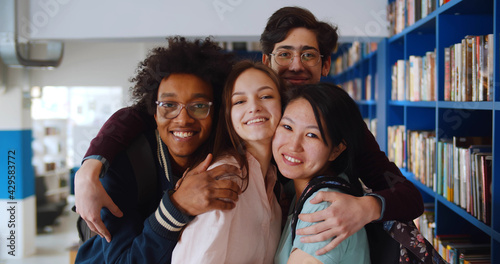 Slika na platnu Portrait of happy multiethnic young people posing at camera in school library