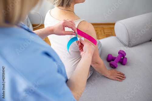 Young woman wearing blue and pink kinesio therapy tape on her shoulder. Alternative medicine rehab. Woman having shoulder physical therapy with kinesiotaping