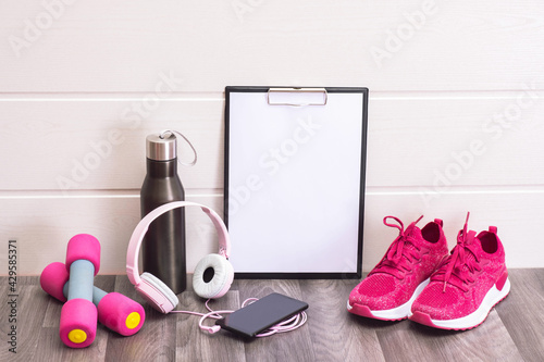 workout equipment at home - pink sneakers, dumbbells, water bottle and note board, headphones and cell phone