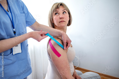 Kinesiology taping. Physical therapist applying kinesiology tape to patient neck. Therapist treating injured trapezius muscles of young athlete. Post traumatic rehabilitation  sport physical therapy.