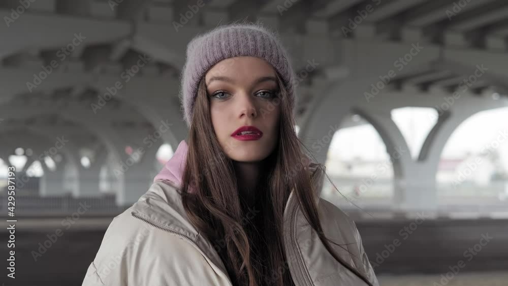 Young woman looking at camera. Female face with red lips. Gorgeous fashionable model posing with bridge at background. Close-up in 4K, UHD Young woman looking at camera. Female face with red lips. Gorgeous fashionable model posing with bridge at background. Close-up in 4K, UHD
