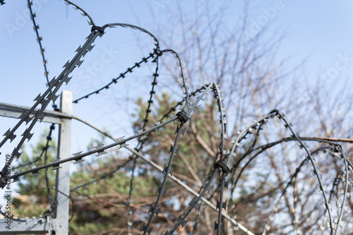 barbed wire on the fence of the restricted area against the background of the sky and trees