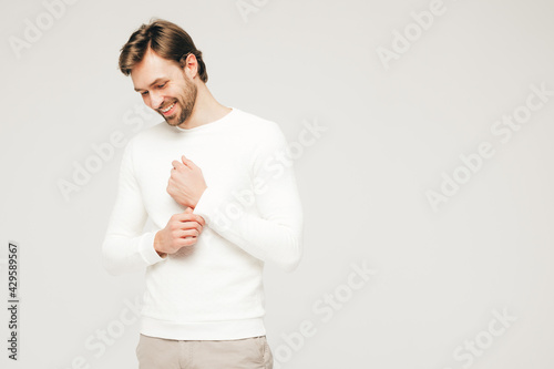 Portrait of handsome smiling hipster lumbersexual businessman model wearing casual white sweater and trousers. Fashion stylish man posing against gray background in studio