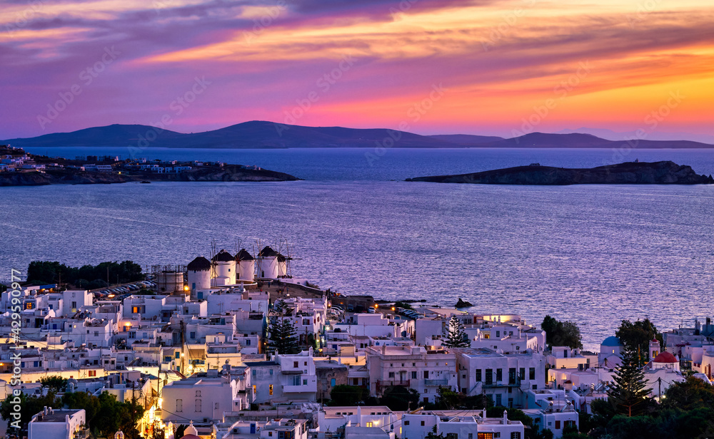 Beautiful sunset view of famous traditional white windmills on hilltop, Mykonos, Greece. Whitewashed houses, sunset sky, summer, town lights on