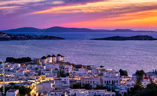 Beautiful sunset view of famous traditional white windmills on hilltop, Mykonos, Greece. Whitewashed houses, sunset sky, summer, town lights on