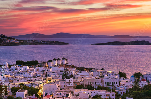 Beautiful sunset view of famous traditional white windmills on hilltop, Mykonos, Greece. Whitewashed house, colorful sunset sky, summer, town light on
