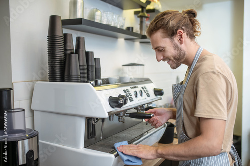 Man in profile wiping coffee machine in cafe
