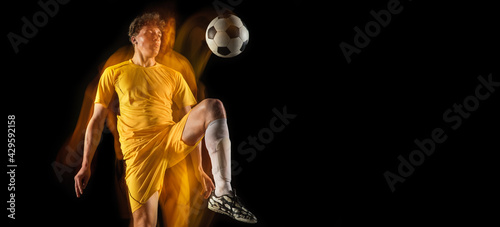 Young caucasian male football or soccer player kicking ball for the goal in mixed light on dark background. Concept of healthy lifestyle, professional sport, hobby.