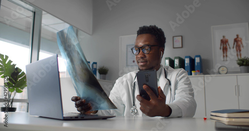 African md wearing white coat and stethoscope, communication with patient via video chat on phone photo