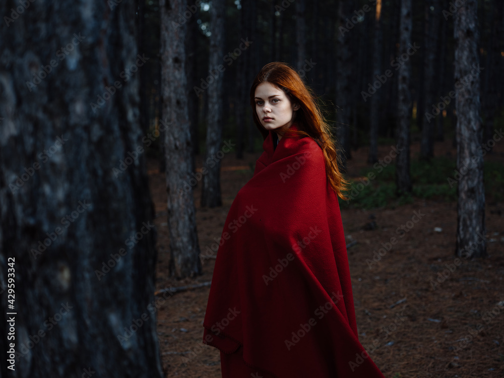 A red-haired woman with a plaid on her shoulders walks in the forest near the trees A red-haired woman with a plaid on her shoulders walks in the forest near the trees