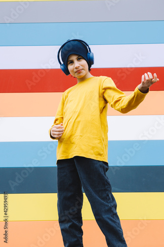 Hispanic teenager with headphones listening to music, dancing on Berlin streets with bright colorful striped background. Copy space.