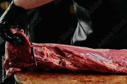 Chef in black gloves cuts raw Tenderloin. fresh raw beef tenderloin on a wooden cutting board. 