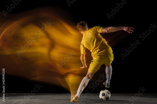 Fototapeta Naklejka Na Ścianę i Meble -  Young caucasian male football or soccer player kicking ball for the goal in mixed light on dark background. Concept of healthy lifestyle, professional sport, hobby.