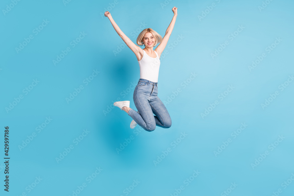 Full size portrait of delighted cheerful person hands fists up beaming smile isolated on blue color background Full size portrait of delighted cheerful person hands fists up beaming smile isolated on blue color background
