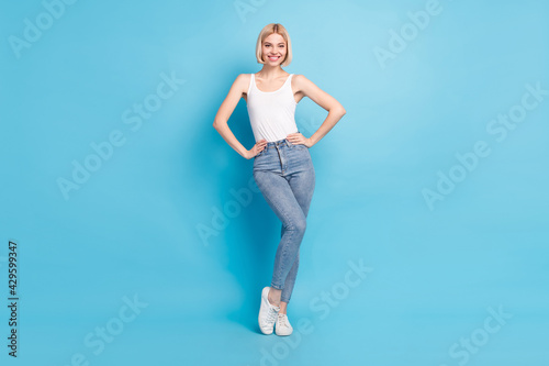 Full size photo of gorgeous satisfied young girl standing put hands on waist toothy smile isolated on blue color background