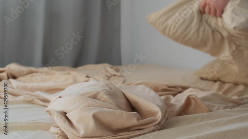 Man makes up his bed in the morning in the bedroom, closeup view. He carefully spreads the duvet cover on the bed. Household chores, daily routine in the morning. Man makes his bed by himself.
