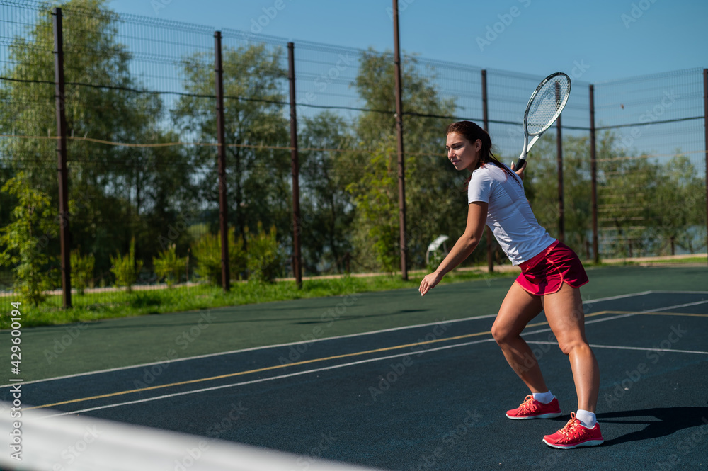 Young caucasian woman playing tennis on an outdoor court on a hot summer day.