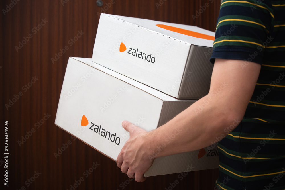 A man carrying/ delivering Zalando boxes in front of the door. Photos |  Adobe Stock