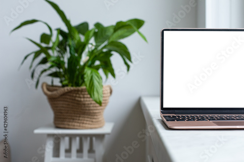 Laptop with blank white screen on the desk, mock up. Personal laptop computer on wood table in living room with modern interior.