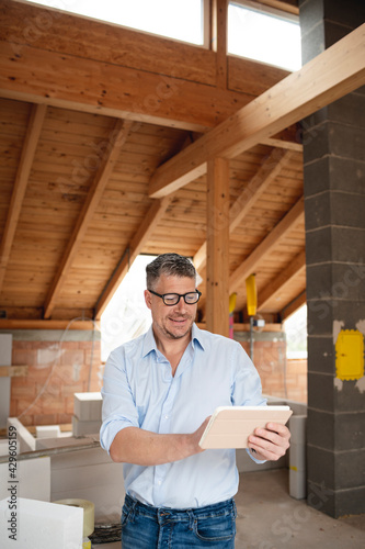 male architect middle age with black glasses stands on construction site in loft house and holds his tablet